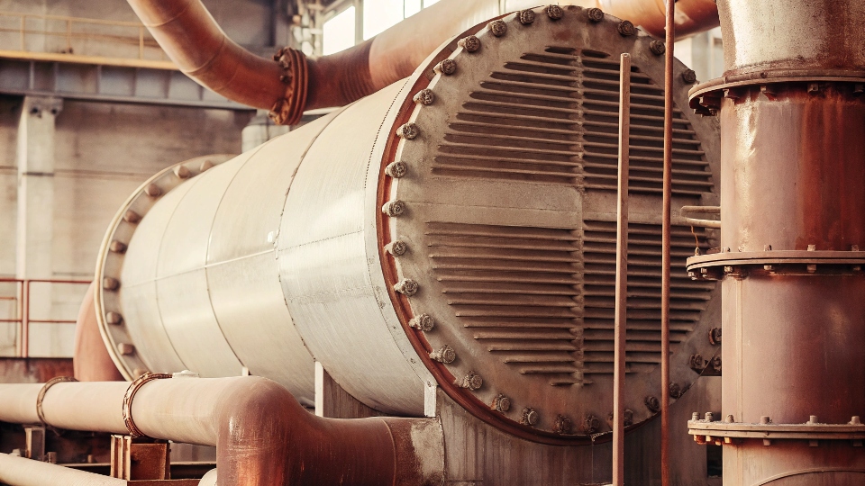 A large industrial titanium heat exchanger with complex piping in a chemical plant setting.