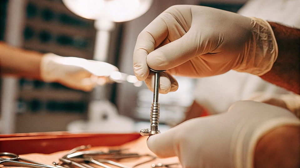 A surgeon carefully handling a small titanium bone screw with sterile instruments.