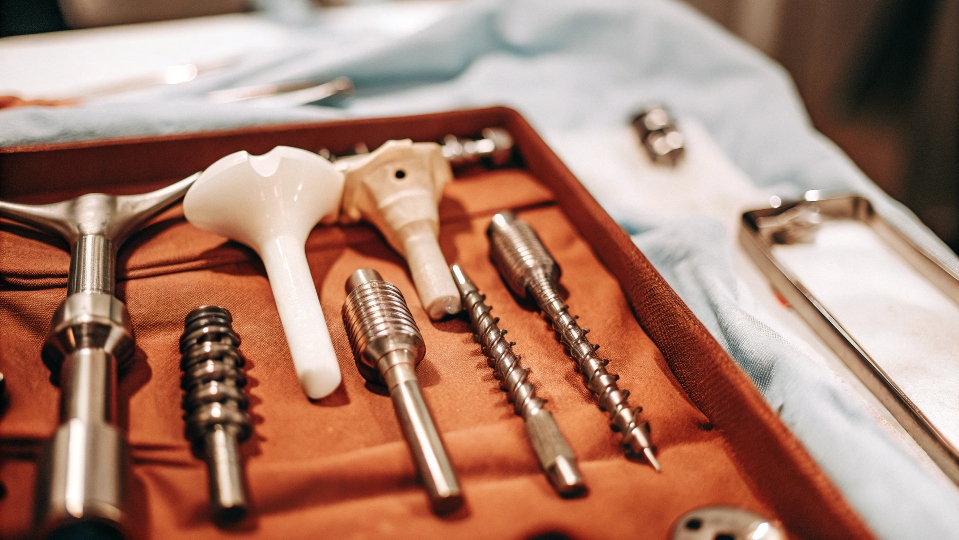An array of different medical implants on a sterile blue cloth, including a hip joint, bone screws, and a dental implant.