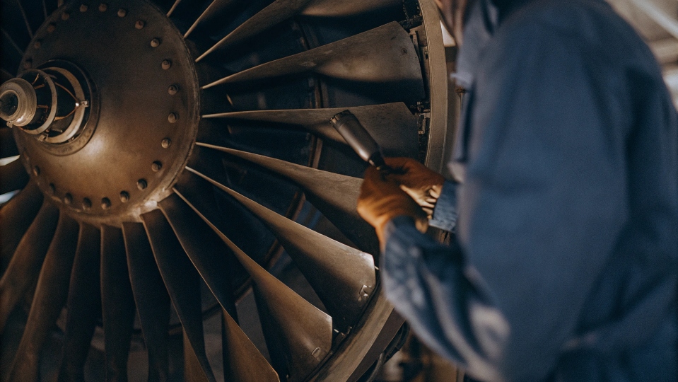 An aerospace engineer inspecting a titanium part on an aircraft engine