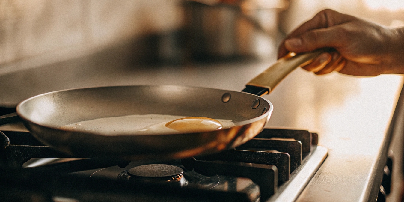 A hand tilting a titanium pan to show an egg sliding off easily.