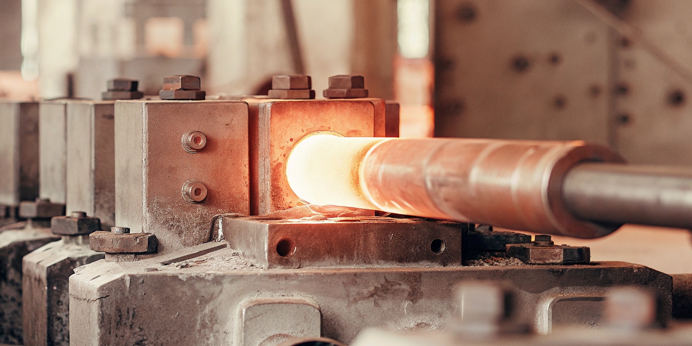 A glowing orange titanium billet being positioned in a large industrial forging press.